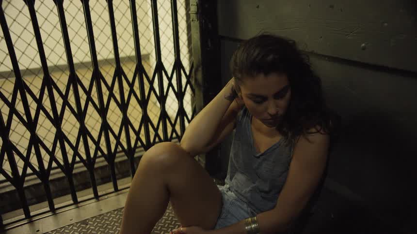 A depressed woman sitting the floor of a lift as it descends through a building