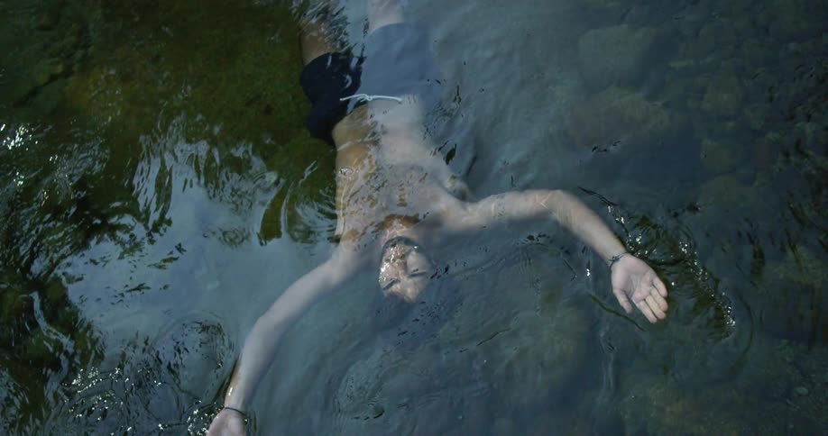 A man floats on his back in a lake moving his arms to stay afloat and letting his face go under