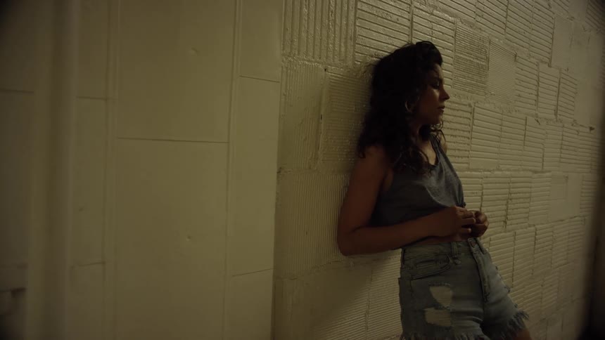 A teenager leans against a brick wall and plays with her shirt