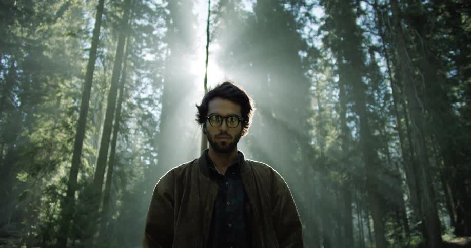 Man stands while the sun shines through the trees in the forest