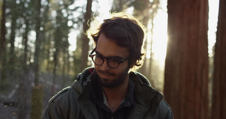 A man standing in a forest with trees and the sun in the background