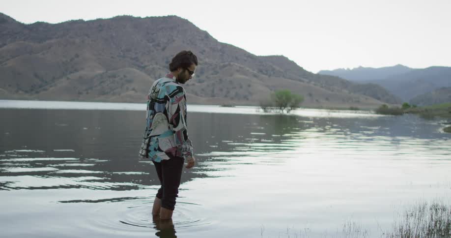 A fully clothed man stand in a lake and looks around