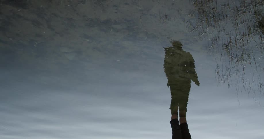 A man stands in water with his reflection showing