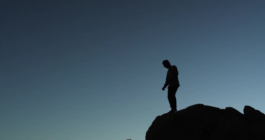 A man carefully walks barefoot at the top of a cliff