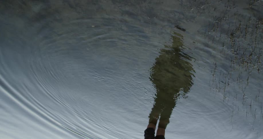 A person looks at their reflection in the water