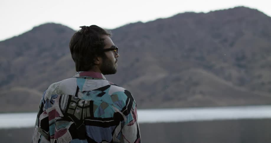 A man standing with a lake and mountain in the background