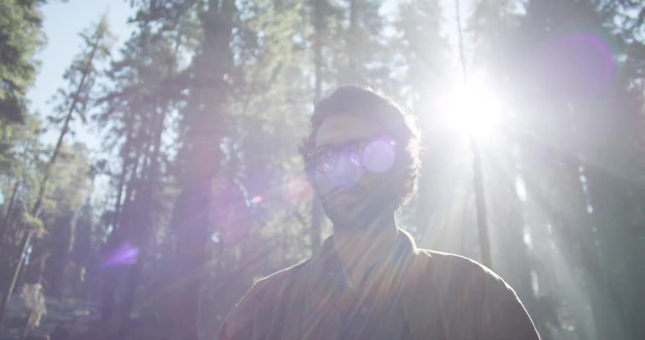 Man standing in the forest with sun beaming through the trees behind him