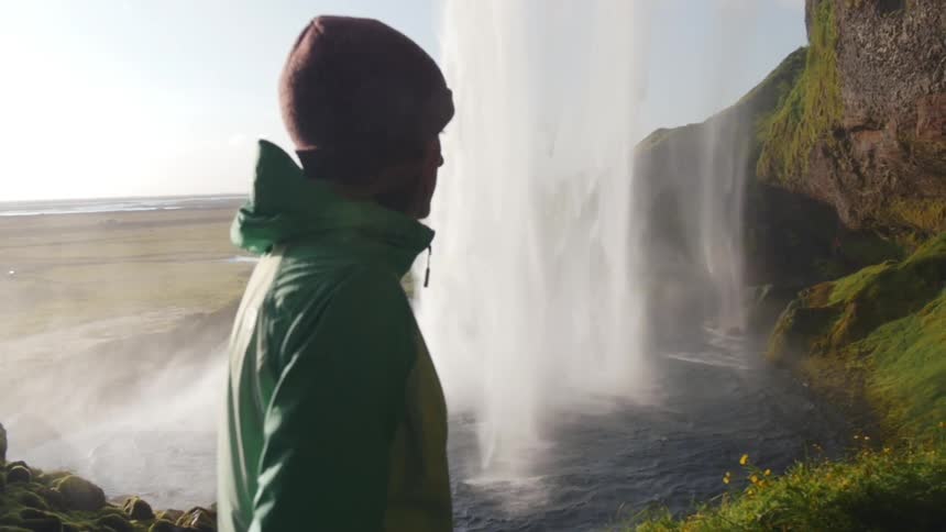 A woman is walking past a waterfall on a sunny day