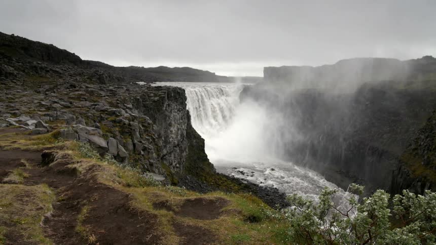 A large waterfall is spraying mist all over the area