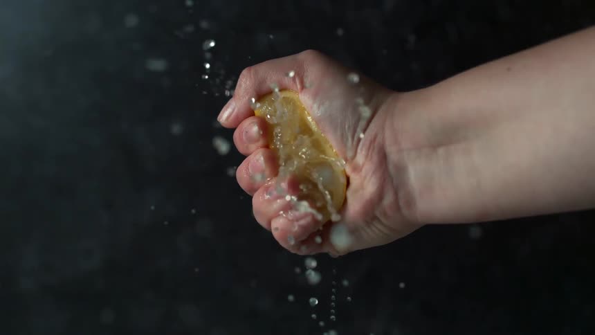 A woman squeezes a lemon until juice squirts out