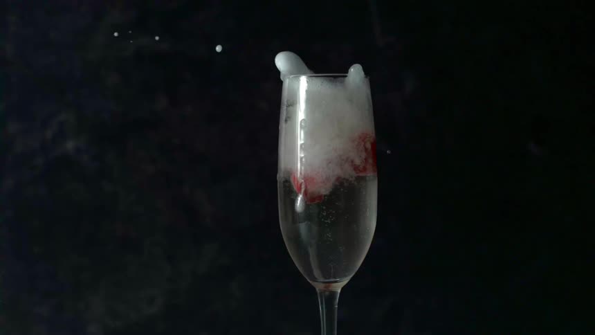 A champagne glass full of champagne and strawberries with a strawberry falling into it