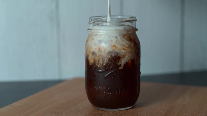 Cream being poured in to an iced coffee