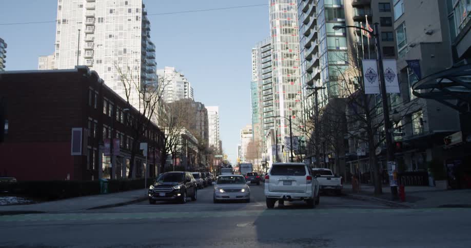 A vehicle turns onto a city street that passes by tall buildings