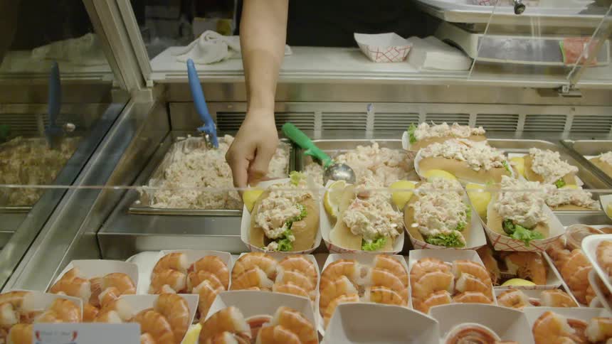A woman reaches for a sandwich at a counter