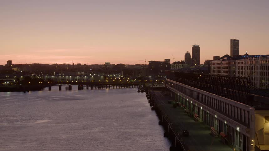 Cars travel over a bridge near an empty waterfront boardwalk with city skyline behind