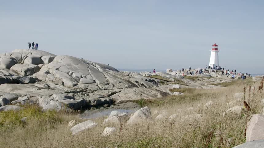 A group of people walk around a lighthouse on the shore
