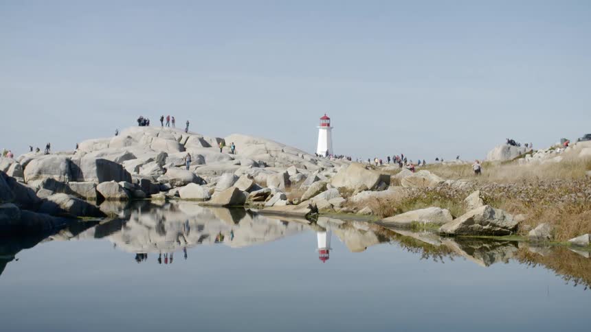 People walk around the lighthouse surrounded by rocks