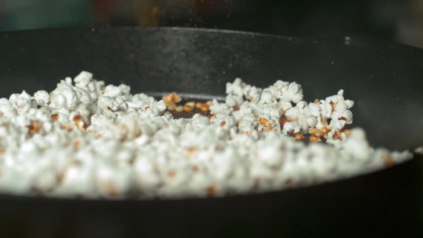 Salt sprinkles down on popcorn in a cast iron pan