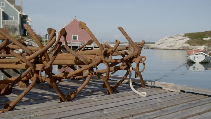 Old rusted anchors stacked on a wooden pier near a body of water