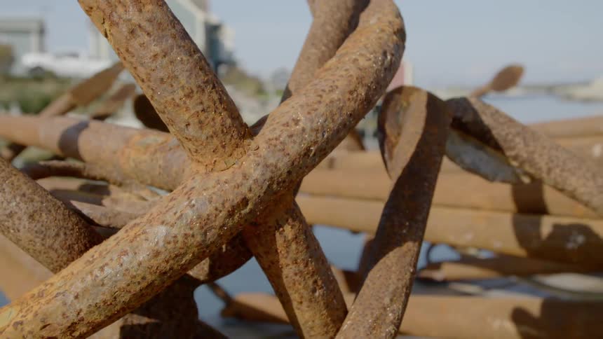 A pile of rusted metal bars sits in a pile near homes and a body of water