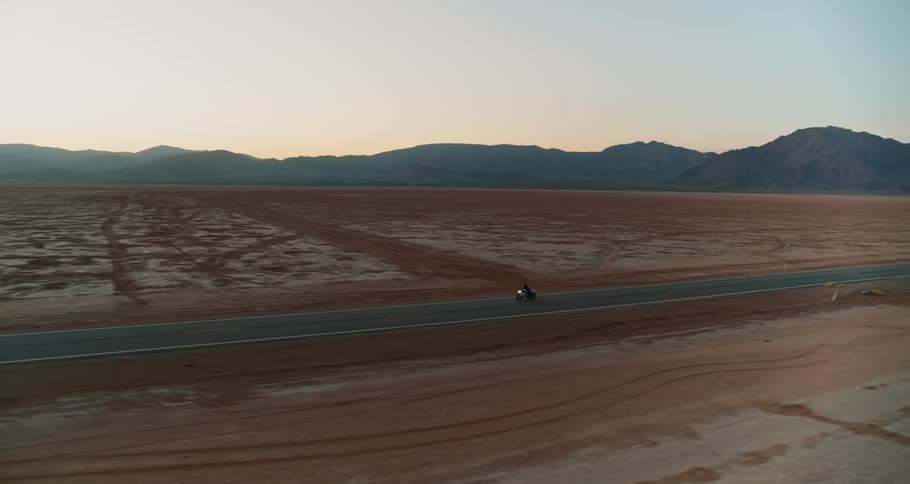Lone motorcycle driving across the desert at sunset