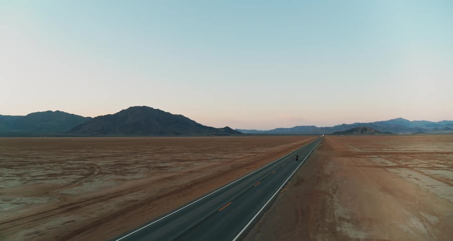Lone motorcycle traveling through the desert on highway at sunset