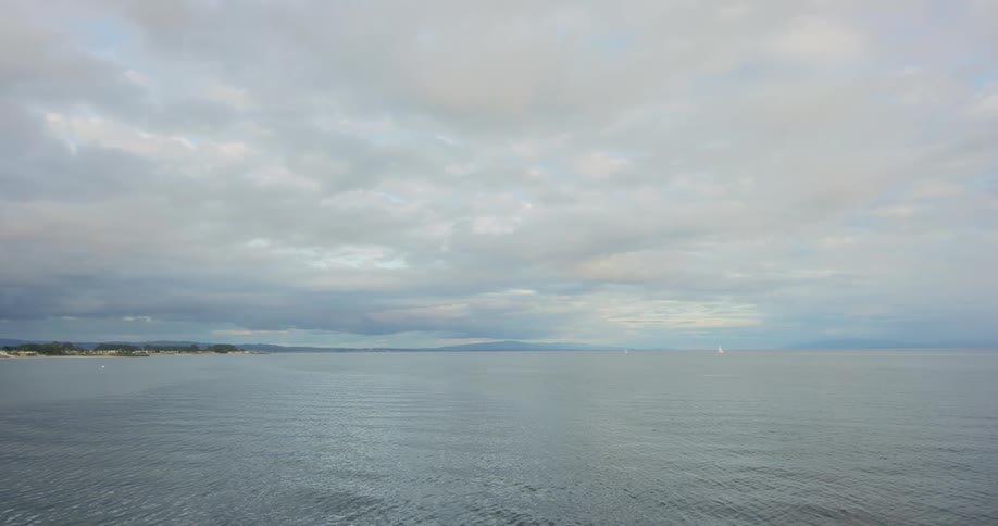 Far away coast and mountains in front of calm sea waves under cloudy sky