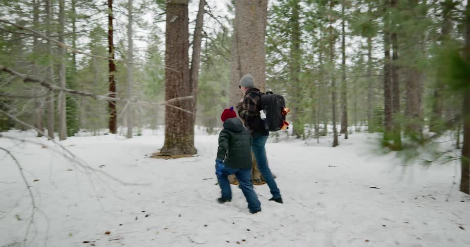 A man and child walk through a snow covered woods area