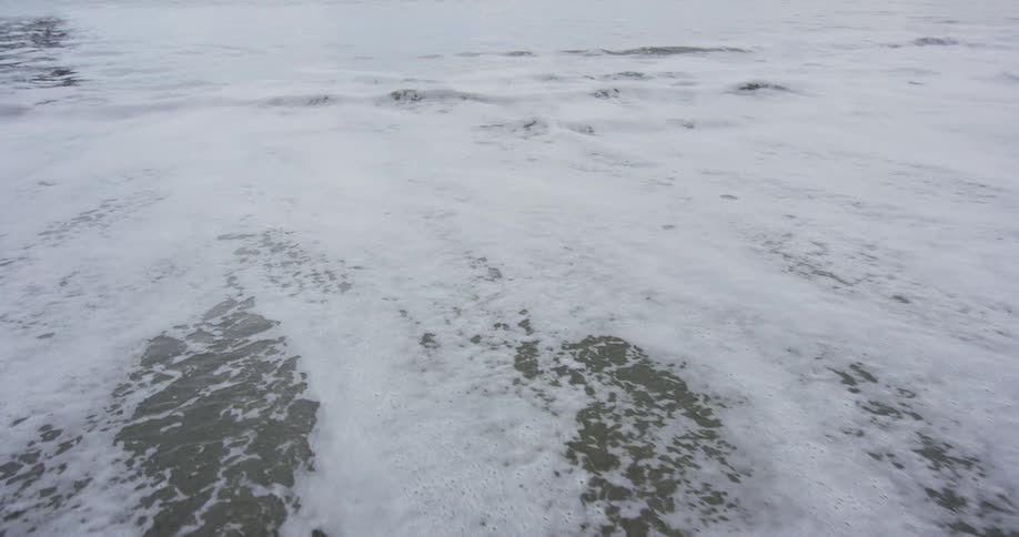 A wave curls and breaks as if comes to a sandy beach shore