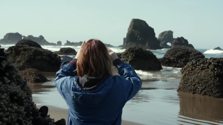 A woman using a cellphone to record the scene at a rocky shoreline