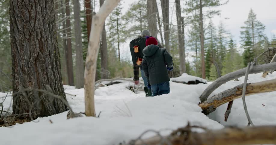 A white man and child walk through a snowy forest