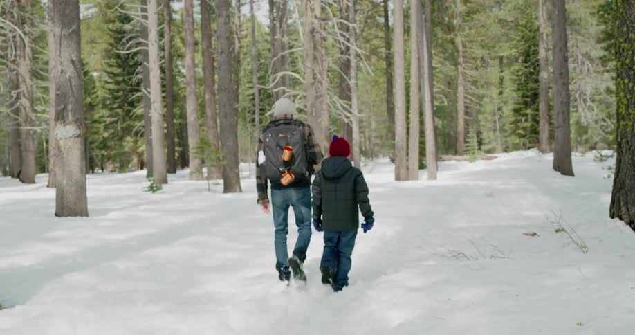 A man and child hike through a snow covered woods area