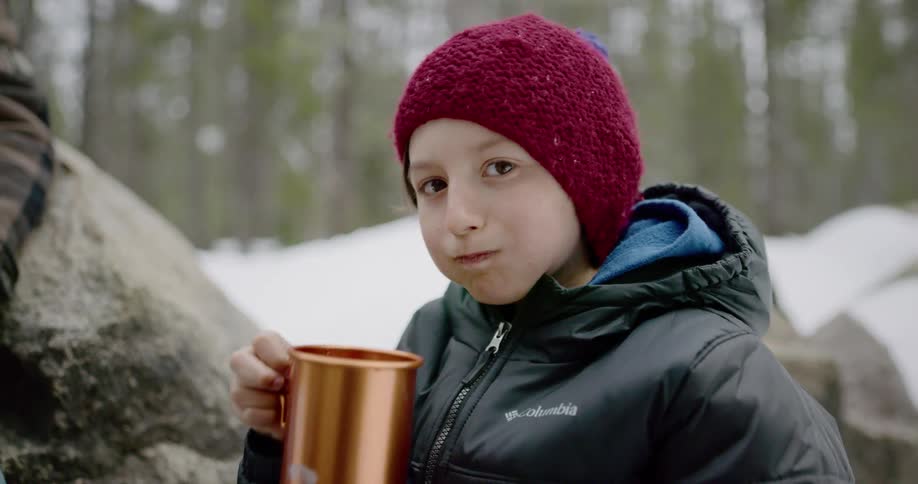A little boy drinks out of a mug while sitting outside