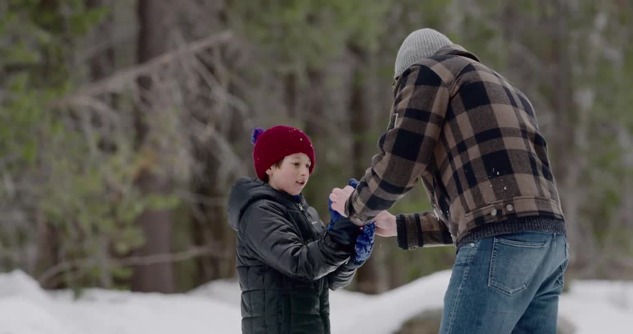 Father helping son out on snow gloves outdoors in the mountains