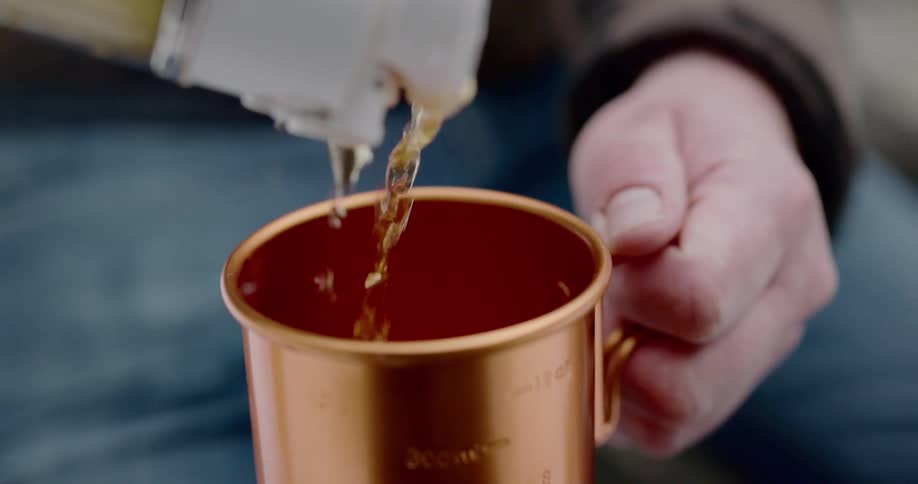 A man pours a drink into a copper moscow mule mug