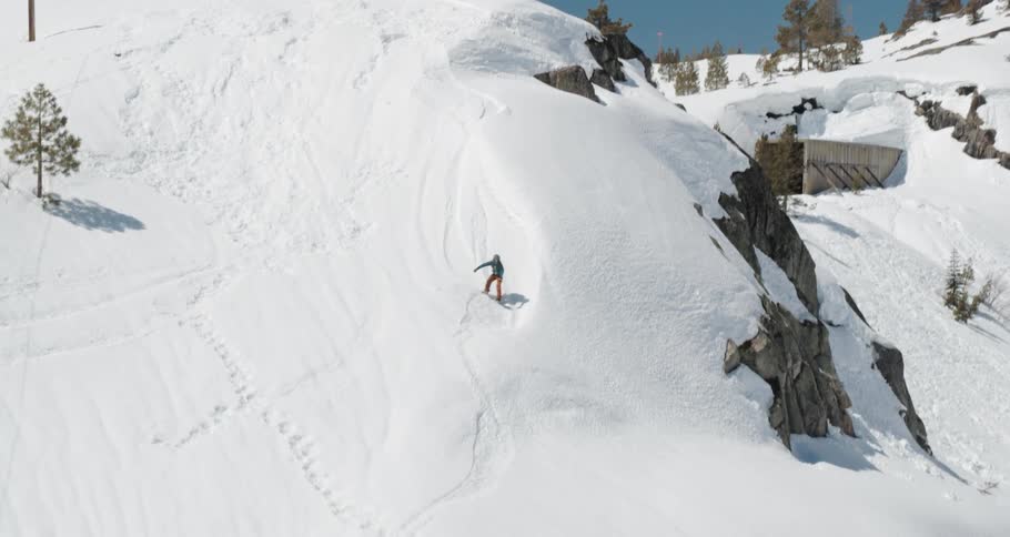A snowboarder boards down a mountain slope on a bright sunny day