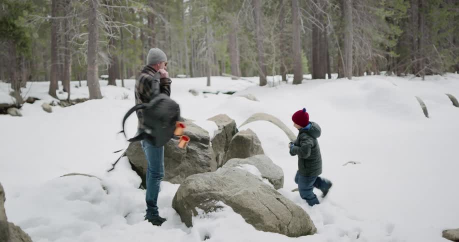 Father and son take a break and sit on a rock in the snow covered woods