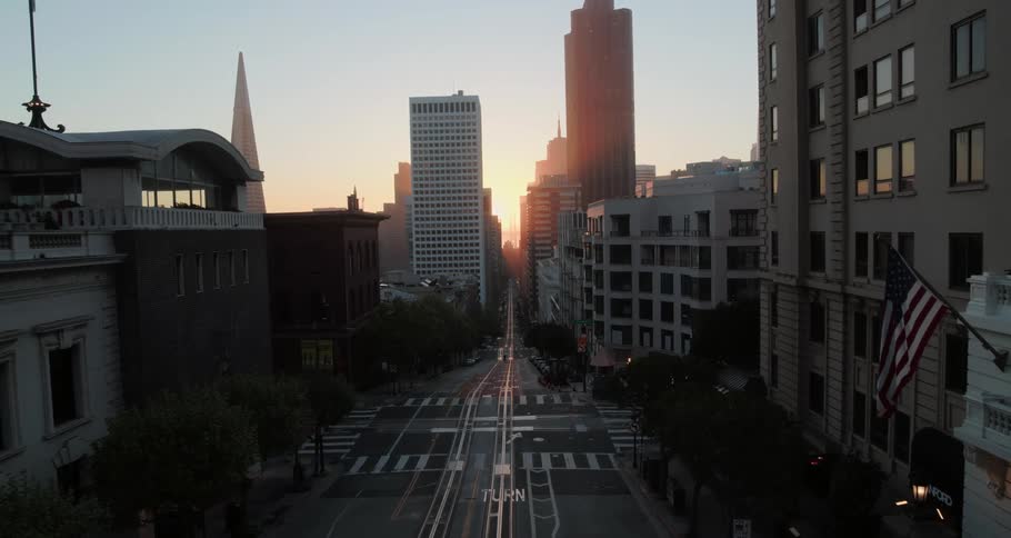 An aerial view down a road in a city at dawn with the camera backing away further down the road