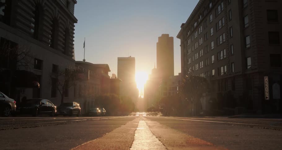 The sun rises between two high rise buildings in a city