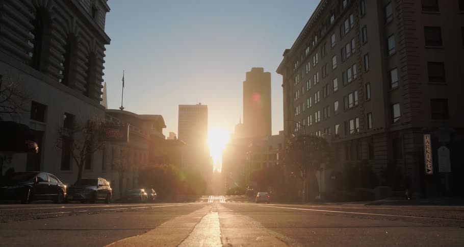 Cars and people on a city street as the bright sun sets