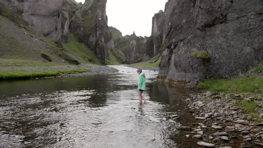A woman wades across a stream in the wilderness