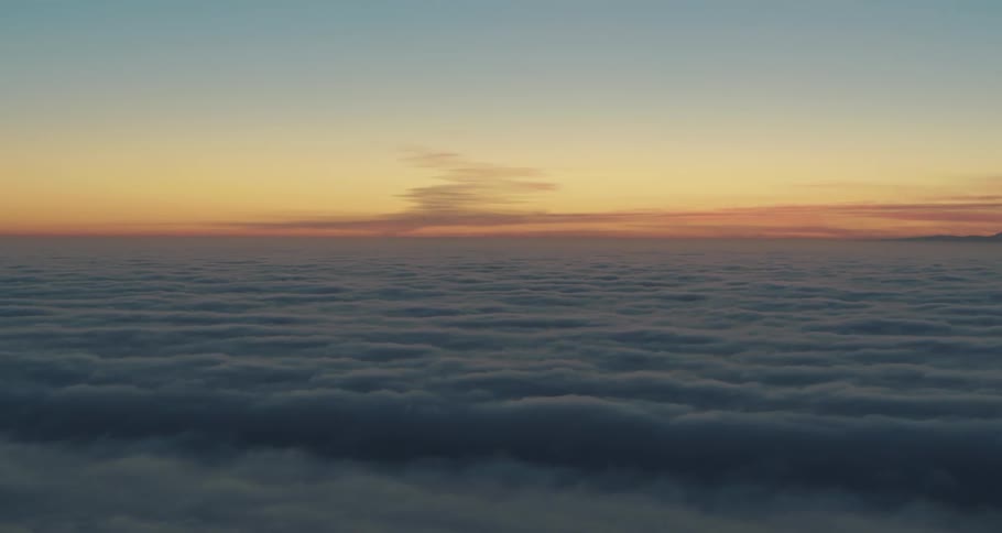 The sun starts to rise and the sky is tinted blue and orange over fluffy clouds