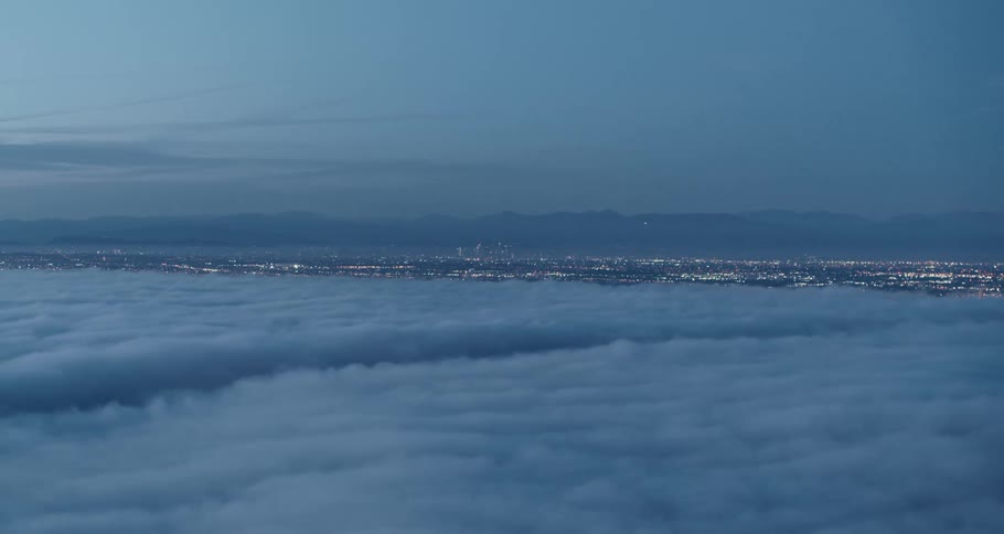 Aerial view above the clouds of a distant downtown city at night