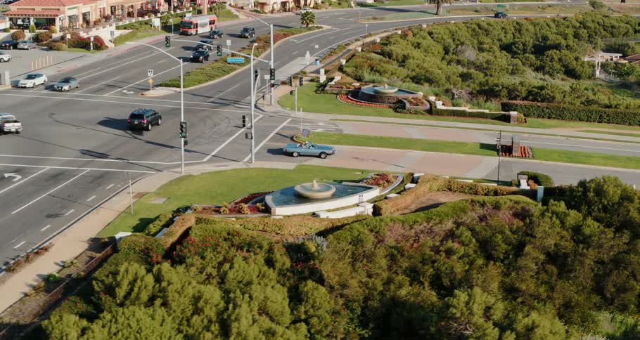 Cars drive through intersection near large fountains