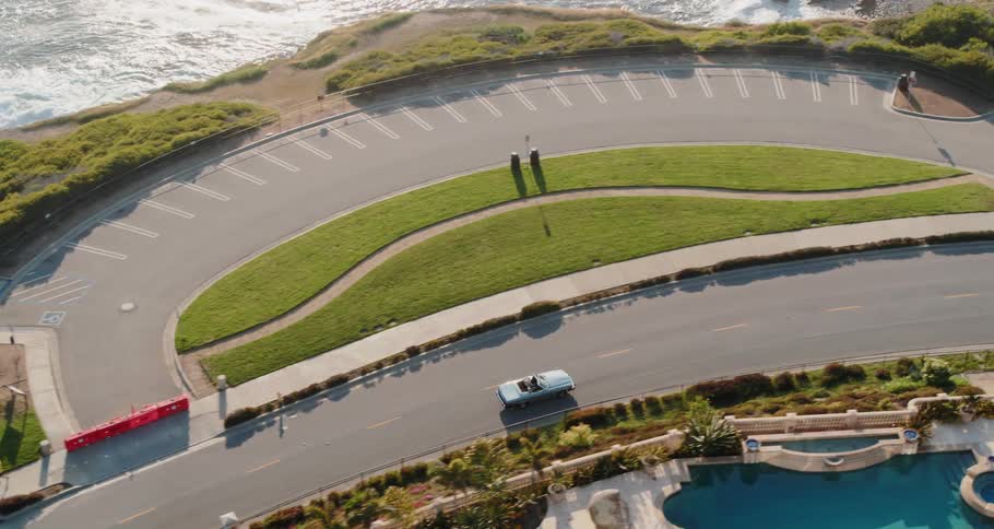 White car travels on the winding road with the ocean below
