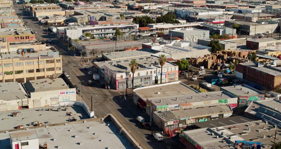 Trucks travel on mainly empty city streets past closed stores and offices on a sunny day
