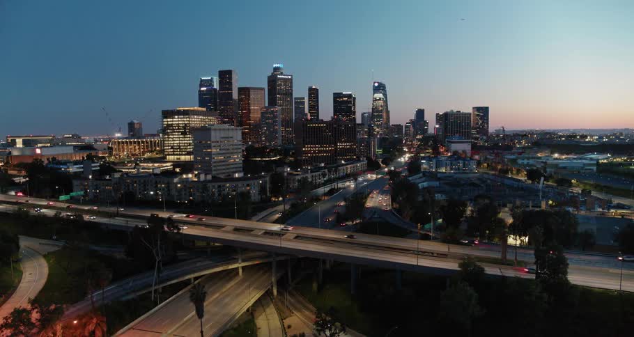 Aerial view of illuminated high rise buildings and vehicles moving along roads at dusk