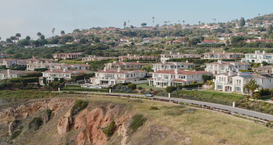 A car travel on a cliff side road with a neighborhood of homes and palm trees on a sunny day