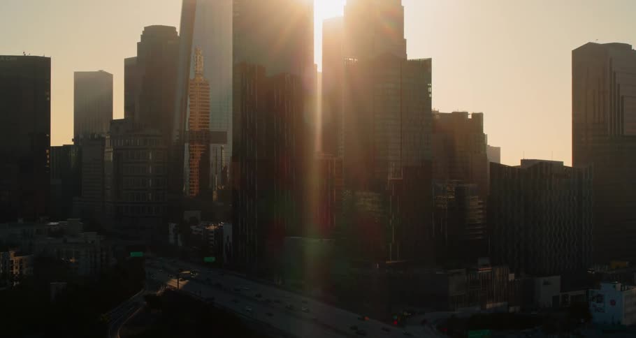Sun shines in orange tinted sky between skyscrapers as fog covers horizon
