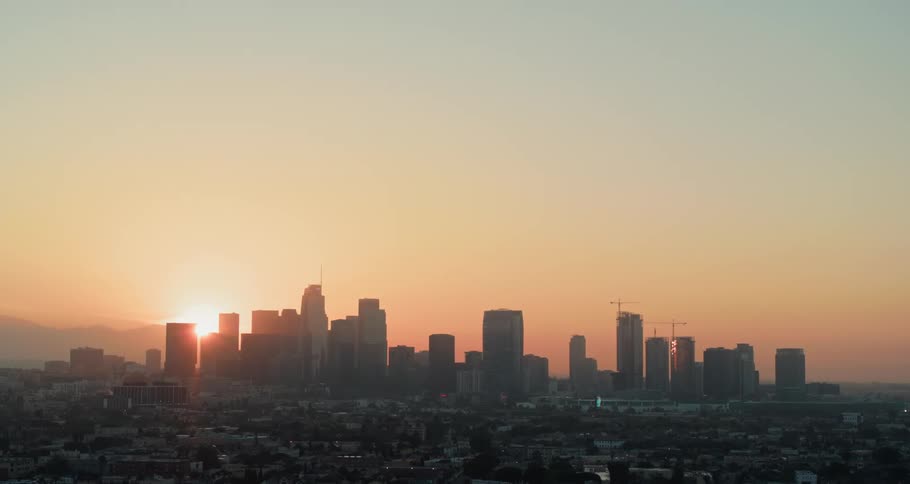 The sun peaking from behind mountains and the skyline of a metropolis